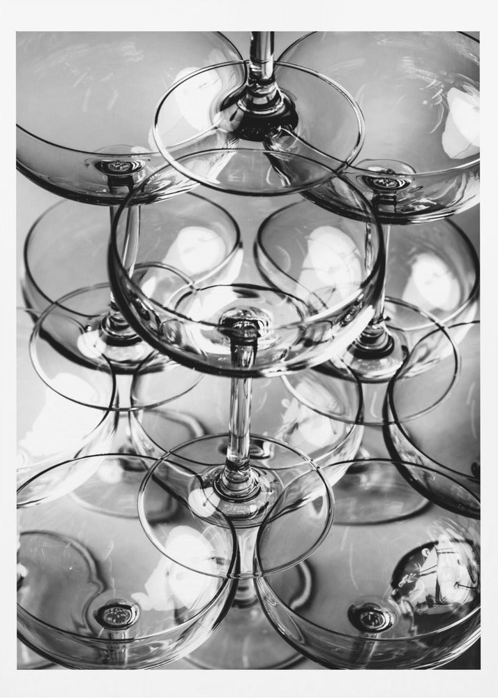 A black and white, overhead photograph of a tightly packed stack of empty champagne coupe glasses. The overlapping rims, stems, and bowls create a complex abstract pattern of circles and reflections, all enclosed within a simple black frame. Poster
