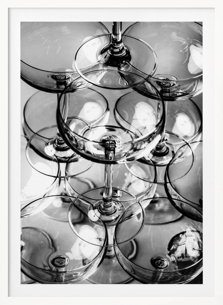 A black and white, overhead photograph of a tightly packed stack of empty champagne coupe glasses. The overlapping rims, stems, and bowls create a complex abstract pattern of circles and reflections, all enclosed within a simple black frame. Poster