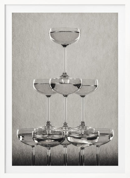 A classic black and white photograph of a champagne tower, with coupe glasses stacked in a pyramid. The glasses are filled with bubbly liquid, and the composition is set against a textured light gray background and enclosed in a black frame. Poster