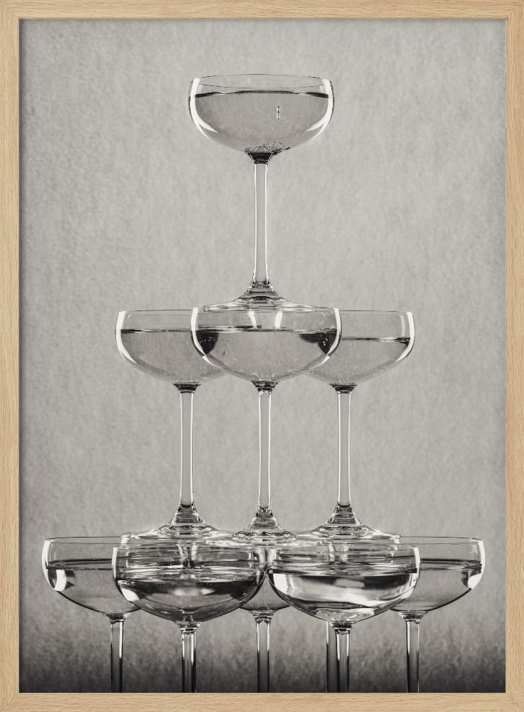 A classic black and white photograph of a champagne tower, with coupe glasses stacked in a pyramid. The glasses are filled with bubbly liquid, and the composition is set against a textured light gray background and enclosed in a black frame. Poster