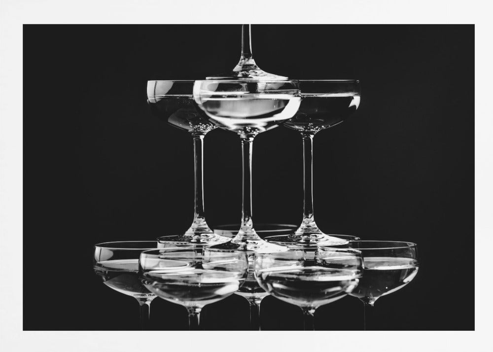 A black and white photograph of a champagne tower made of coupe glasses stacked in a pyramid shape against a solid black background, all within a silver frame. Print
