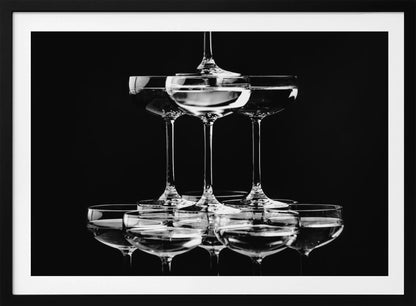 A black and white photograph of a champagne tower made of coupe glasses stacked in a pyramid shape against a solid black background, all within a silver frame. Print