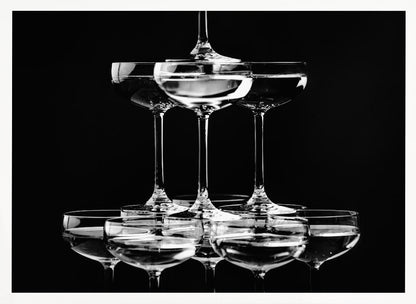 A black and white photograph of a champagne tower made of coupe glasses stacked in a pyramid shape against a solid black background, all within a silver frame. Print