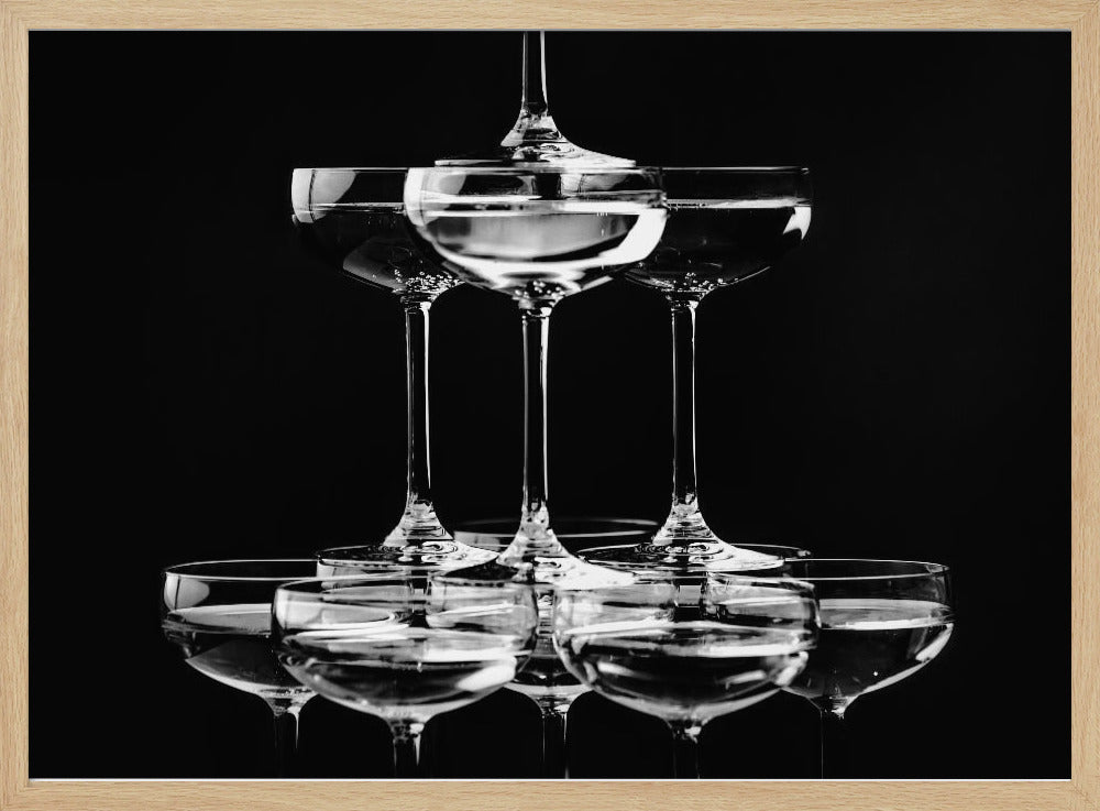 A black and white photograph of a champagne tower made of coupe glasses stacked in a pyramid shape against a solid black background, all within a silver frame. Print