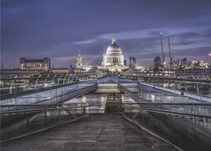 A nighttime photograph from the Millennium Bridge leading towards the brightly illuminated St. Paul's Cathedral against a dark blue twilight sky in London, all enclosed in a silver frame. Poster