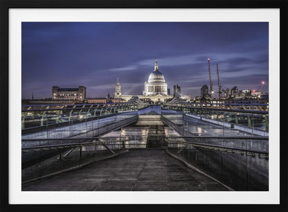 A nighttime photograph from the Millennium Bridge leading towards the brightly illuminated St. Paul's Cathedral against a dark blue twilight sky in London, all enclosed in a silver frame. Poster