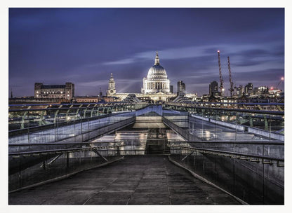 A nighttime photograph from the Millennium Bridge leading towards the brightly illuminated St. Paul's Cathedral against a dark blue twilight sky in London, all enclosed in a silver frame. Poster