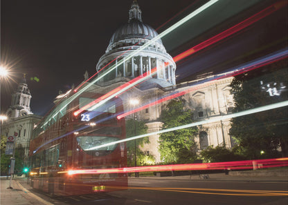 A long-exposure night photograph of a red double-decker bus in London, creating vibrant red and white light trails in front of the illuminated St. Paul's Cathedral. Decor