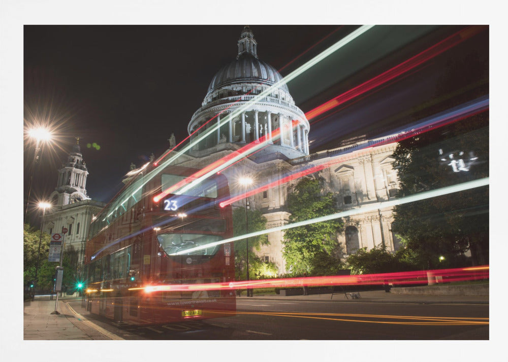 A long-exposure night photograph of a red double-decker bus in London, creating vibrant red and white light trails in front of the illuminated St. Paul's Cathedral. Decor