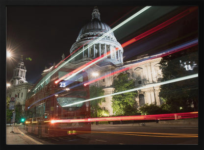 A long-exposure night photograph of a red double-decker bus in London, creating vibrant red and white light trails in front of the illuminated St. Paul's Cathedral. Decor