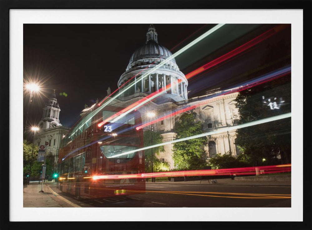 A long-exposure night photograph of a red double-decker bus in London, creating vibrant red and white light trails in front of the illuminated St. Paul's Cathedral. Decor