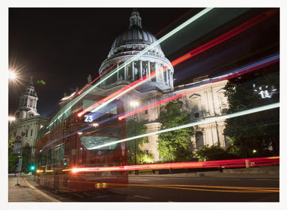 A long-exposure night photograph of a red double-decker bus in London, creating vibrant red and white light trails in front of the illuminated St. Paul's Cathedral. Decor