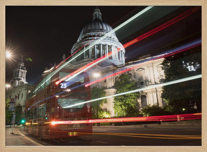 A long-exposure night photograph of a red double-decker bus in London, creating vibrant red and white light trails in front of the illuminated St. Paul's Cathedral. Decor