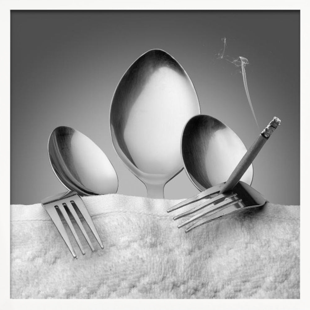 A conceptual black and white photograph in a light wood frame, featuring three spoons standing upright on a white towel, while a fork in the foreground holds a lit, smoking cigarette between its tines. Wall Art