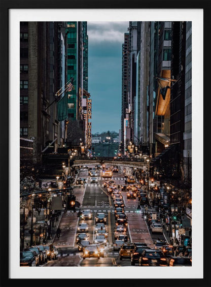 A high-angle, vertical photograph looking down a bustling New York City street at dusk, framed by towering skyscrapers. The street below is packed with cars, their headlights creating a warm golden glow, contrasting with the cool, dark blue tones of the twilight sky and buildings. Poster