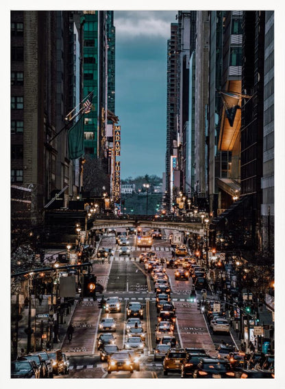 A high-angle, vertical photograph looking down a bustling New York City street at dusk, framed by towering skyscrapers. The street below is packed with cars, their headlights creating a warm golden glow, contrasting with the cool, dark blue tones of the twilight sky and buildings. Poster