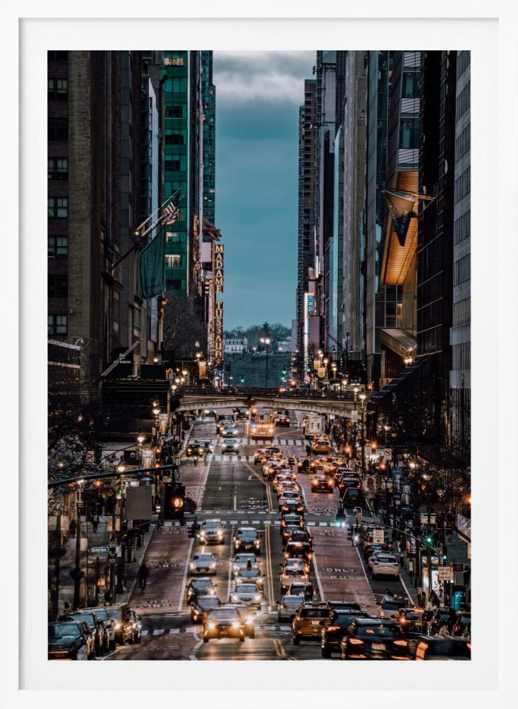 A high-angle, vertical photograph looking down a bustling New York City street at dusk, framed by towering skyscrapers. The street below is packed with cars, their headlights creating a warm golden glow, contrasting with the cool, dark blue tones of the twilight sky and buildings. Poster