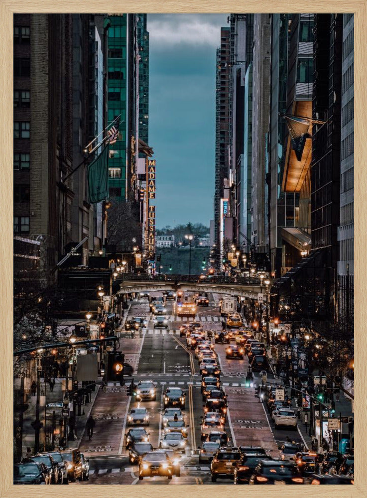 A high-angle, vertical photograph looking down a bustling New York City street at dusk, framed by towering skyscrapers. The street below is packed with cars, their headlights creating a warm golden glow, contrasting with the cool, dark blue tones of the twilight sky and buildings. Poster
