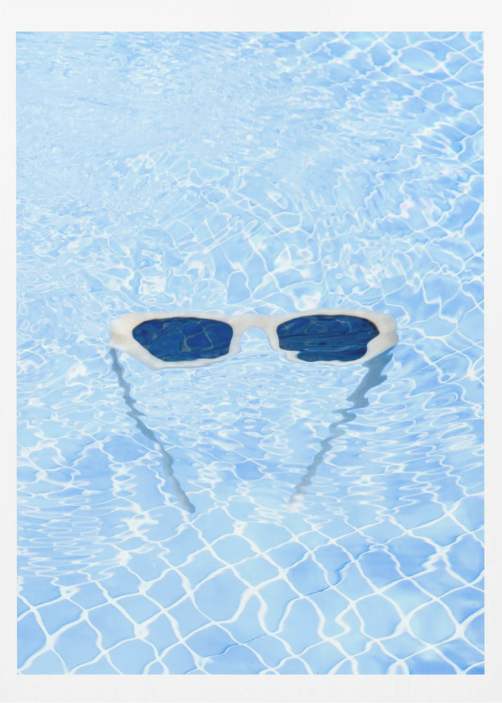 A pair of white-framed sunglasses with dark lenses floats on the surface of a bright blue swimming pool. The rippling water distorts the view of the tiled pool floor, and the sunglasses cast a faint shadow underneath. Print