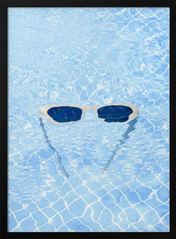 A pair of white-framed sunglasses with dark lenses floats on the surface of a bright blue swimming pool. The rippling water distorts the view of the tiled pool floor, and the sunglasses cast a faint shadow underneath. Print