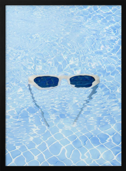 A pair of white-framed sunglasses with dark lenses floats on the surface of a bright blue swimming pool. The rippling water distorts the view of the tiled pool floor, and the sunglasses cast a faint shadow underneath. Print