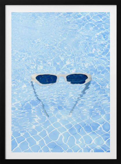 A pair of white-framed sunglasses with dark lenses floats on the surface of a bright blue swimming pool. The rippling water distorts the view of the tiled pool floor, and the sunglasses cast a faint shadow underneath. Print
