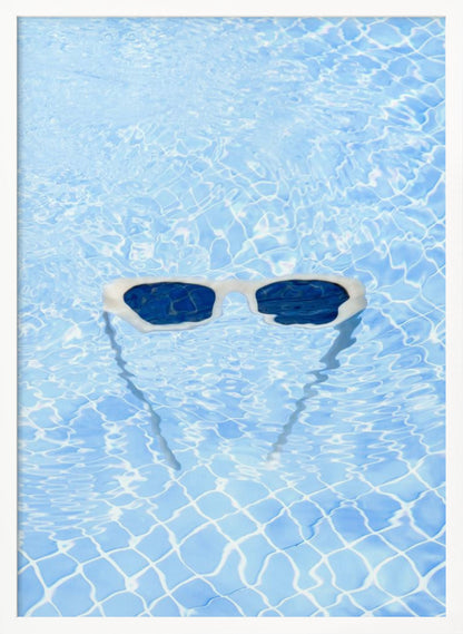A pair of white-framed sunglasses with dark lenses floats on the surface of a bright blue swimming pool. The rippling water distorts the view of the tiled pool floor, and the sunglasses cast a faint shadow underneath. Print
