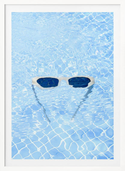 A pair of white-framed sunglasses with dark lenses floats on the surface of a bright blue swimming pool. The rippling water distorts the view of the tiled pool floor, and the sunglasses cast a faint shadow underneath. Print