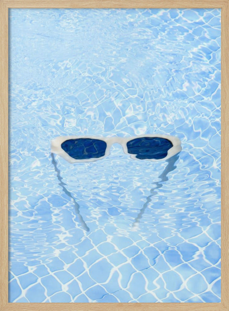A pair of white-framed sunglasses with dark lenses floats on the surface of a bright blue swimming pool. The rippling water distorts the view of the tiled pool floor, and the sunglasses cast a faint shadow underneath. Print