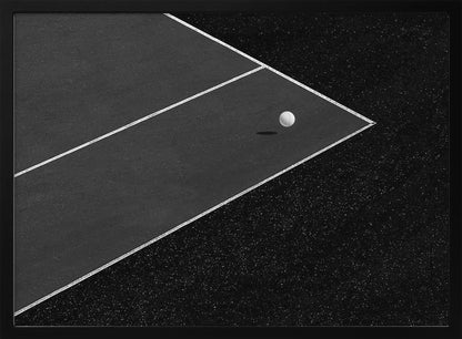 A minimalist black and white overhead photograph of a white ball resting in the corner of a dark tennis or paddle court. The composition focuses on the strong geometric angles created by the white boundary lines against the dark, textured asphalt, all within a silver frame. Artwork