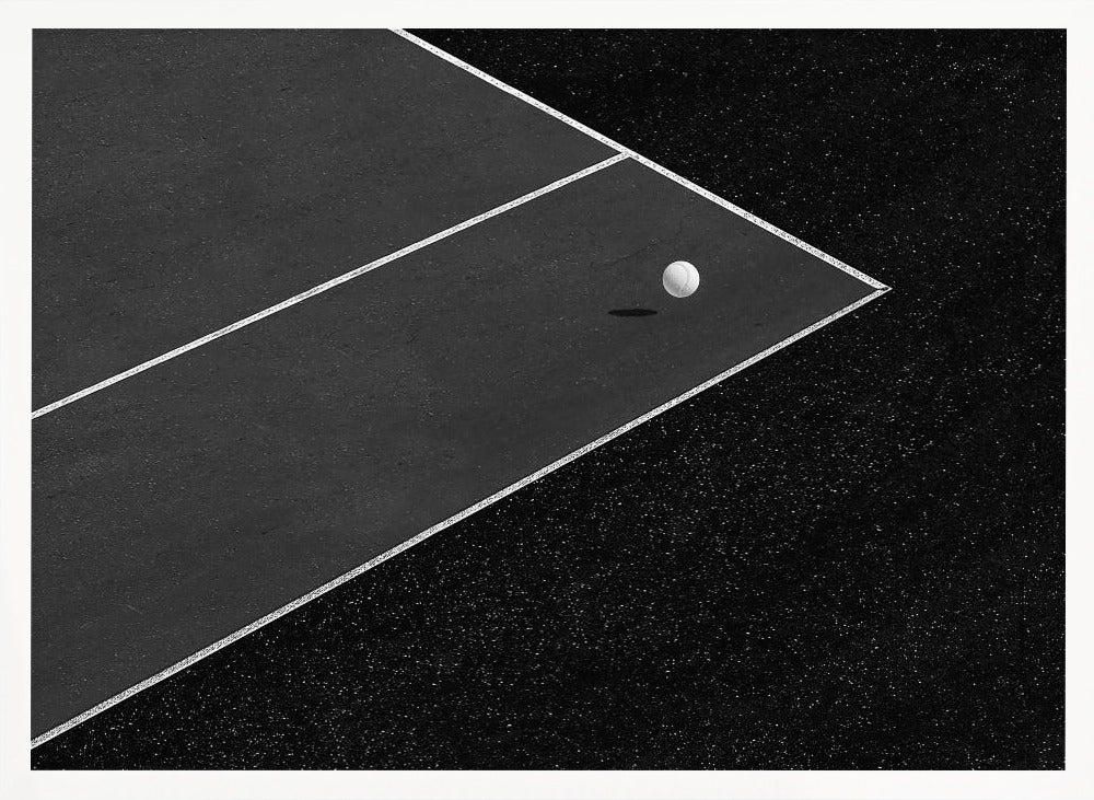 A minimalist black and white overhead photograph of a white ball resting in the corner of a dark tennis or paddle court. The composition focuses on the strong geometric angles created by the white boundary lines against the dark, textured asphalt, all within a silver frame. Artwork