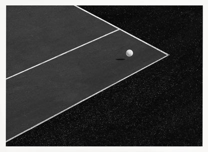 A minimalist black and white overhead photograph of a white ball resting in the corner of a dark tennis or paddle court. The composition focuses on the strong geometric angles created by the white boundary lines against the dark, textured asphalt, all within a silver frame. Artwork