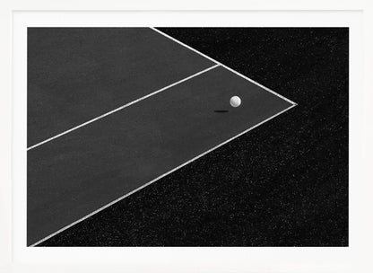 A minimalist black and white overhead photograph of a white ball resting in the corner of a dark tennis or paddle court. The composition focuses on the strong geometric angles created by the white boundary lines against the dark, textured asphalt, all within a silver frame. Artwork