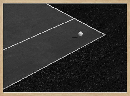 A minimalist black and white overhead photograph of a white ball resting in the corner of a dark tennis or paddle court. The composition focuses on the strong geometric angles created by the white boundary lines against the dark, textured asphalt, all within a silver frame. Artwork