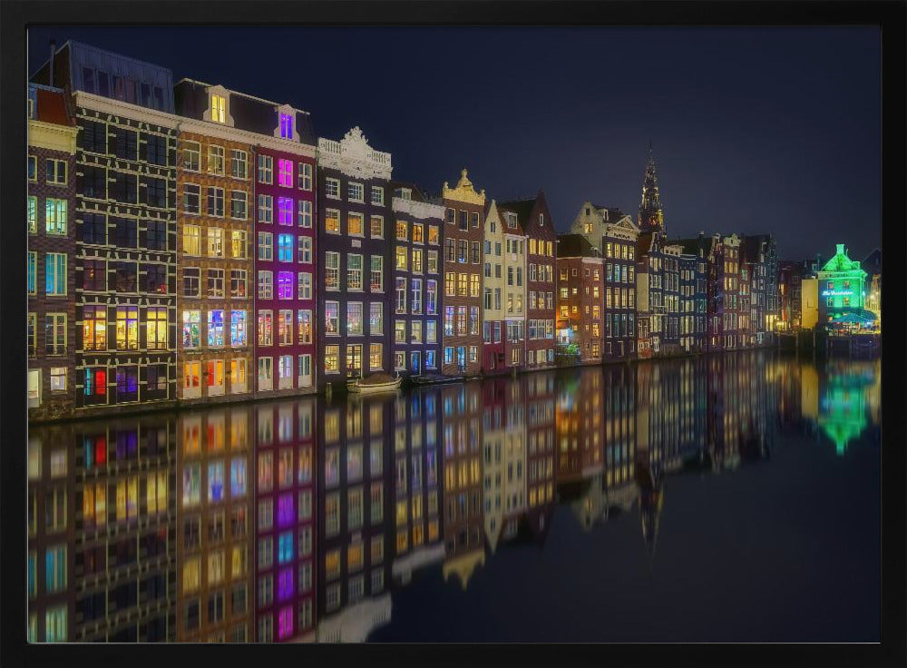 A vibrant nighttime photograph of colorful canal houses in Amsterdam, with their glowing lights beautifully reflected in the still water of the canal below, all framed in silver. Print