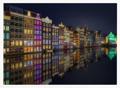 A vibrant nighttime photograph of colorful canal houses in Amsterdam, with their glowing lights beautifully reflected in the still water of the canal below, all framed in silver. Print