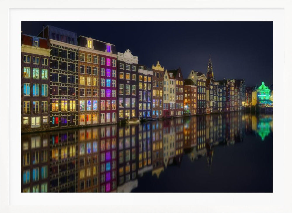 A vibrant nighttime photograph of colorful canal houses in Amsterdam, with their glowing lights beautifully reflected in the still water of the canal below, all framed in silver. Print
