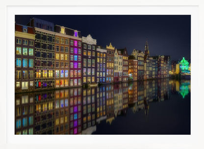 A vibrant nighttime photograph of colorful canal houses in Amsterdam, with their glowing lights beautifully reflected in the still water of the canal below, all framed in silver. Print