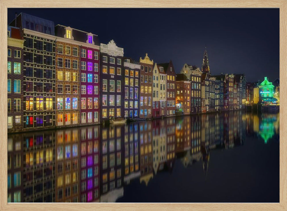 A vibrant nighttime photograph of colorful canal houses in Amsterdam, with their glowing lights beautifully reflected in the still water of the canal below, all framed in silver. Print
