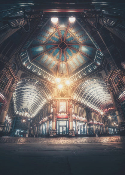 A dramatic, low-angle, wide shot of an empty Leadenhall Market at night. The ornate, domed ceiling is illuminated in blue and gold by bright, warm lights, which also cast a glow on the cobblestone floor and detailed Victorian storefronts. Wall Art