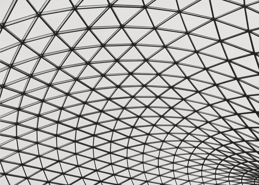 A framed, black and white photograph of a modern architectural dome ceiling. The image is a close-up, looking up at the intricate metal framework that creates a repeating pattern of triangles against the bright glass panels. Poster