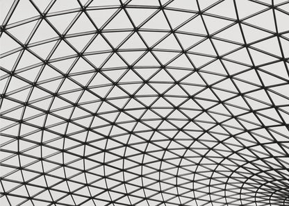 A framed, black and white photograph of a modern architectural dome ceiling. The image is a close-up, looking up at the intricate metal framework that creates a repeating pattern of triangles against the bright glass panels. Poster