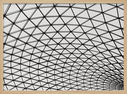 A framed, black and white photograph of a modern architectural dome ceiling. The image is a close-up, looking up at the intricate metal framework that creates a repeating pattern of triangles against the bright glass panels. Poster