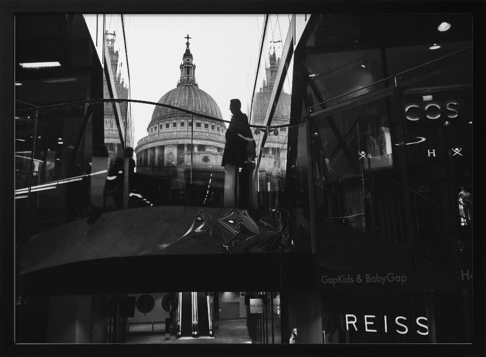 A framed, black and white photograph capturing the reflection of St. Paul's Cathedral in the glass of a modern shopping center. A person's silhouette stands on an interior balcony, juxtaposed against the historic dome, while the mall's interior and store signs are visible in the foreground. Print