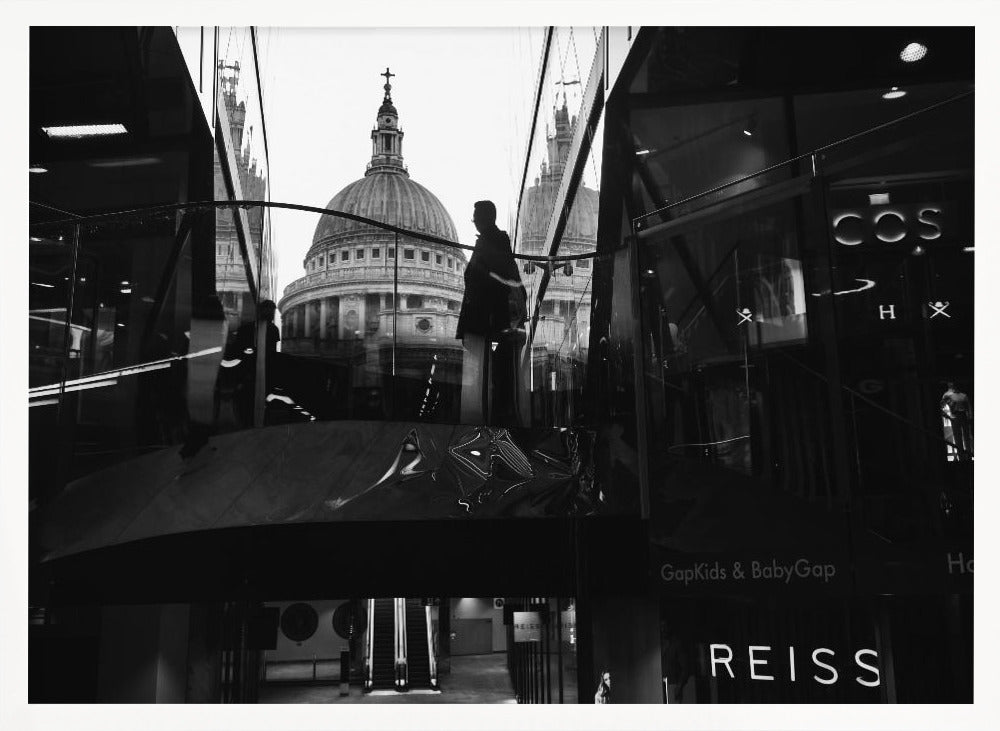A framed, black and white photograph capturing the reflection of St. Paul's Cathedral in the glass of a modern shopping center. A person's silhouette stands on an interior balcony, juxtaposed against the historic dome, while the mall's interior and store signs are visible in the foreground. Print
