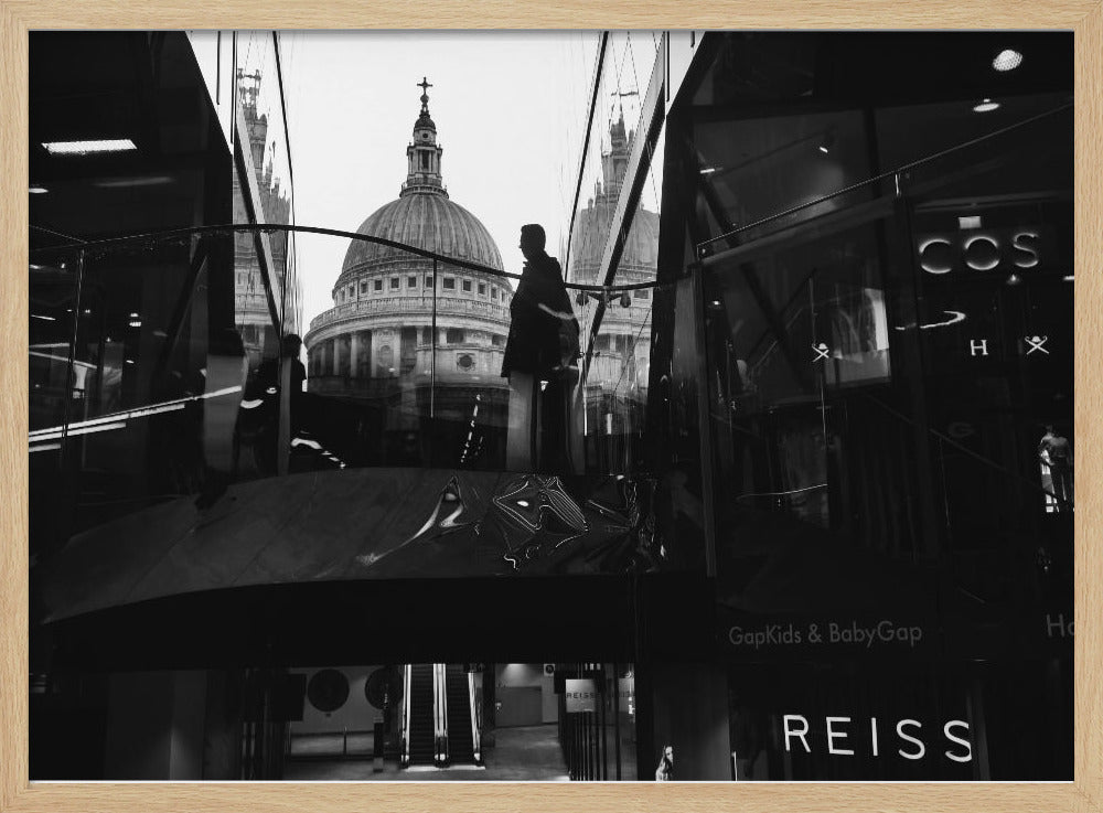 A framed, black and white photograph capturing the reflection of St. Paul's Cathedral in the glass of a modern shopping center. A person's silhouette stands on an interior balcony, juxtaposed against the historic dome, while the mall's interior and store signs are visible in the foreground. Print