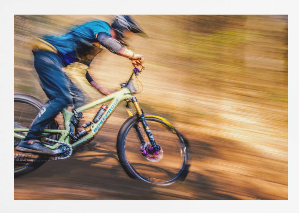 An action shot of a mountain biker in full gear speeding down a dirt trail, captured with a motion blur effect that streaks the brown and green background, conveying a sense of intense speed. Poster
