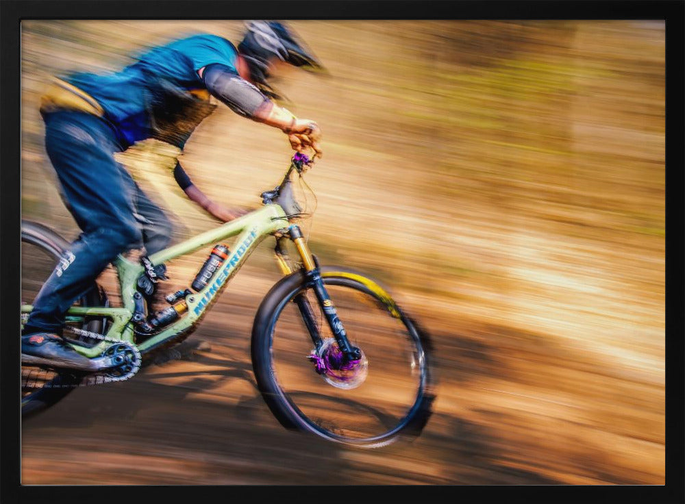 An action shot of a mountain biker in full gear speeding down a dirt trail, captured with a motion blur effect that streaks the brown and green background, conveying a sense of intense speed. Poster