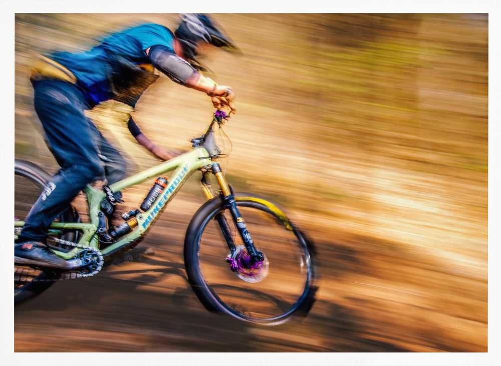 An action shot of a mountain biker in full gear speeding down a dirt trail, captured with a motion blur effect that streaks the brown and green background, conveying a sense of intense speed. Poster