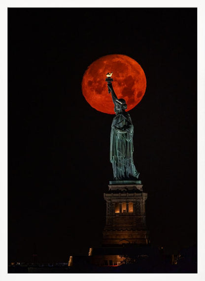 A striking night photograph of the Statue of Liberty perfectly silhouetted against a giant, vibrant red supermoon, which appears to be held aloft by the statue's torch against a deep black sky. Artwork